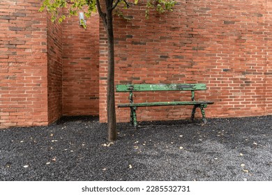 An old green bench stands next to a green tree in front of a brick wall on a stone chipping background - Powered by Shutterstock