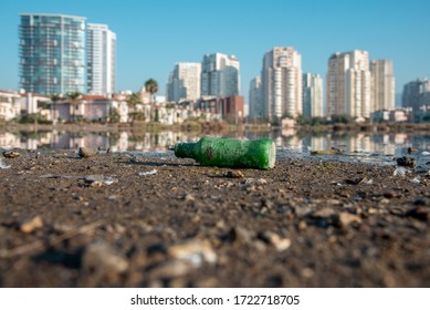 An Old Green Soda Bottle Above Ground. Buildings Reflection Background.