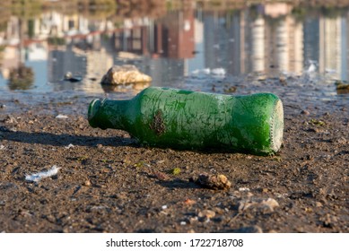 An Old Green Soda Bottle Above Ground. Buildings Reflection Background.