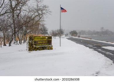 Old Greenwich, CT, USA-August 2020: View of the snow covered entrance of Greenwich Point Park or Tods Point with large sign next to road and American flag with heavy snow falling
