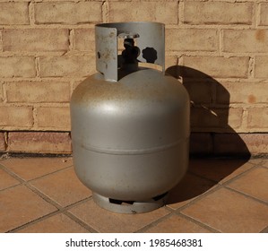 Old Grey Rusting Gas Bottle On A Sunny Day With Beige Brick Background.