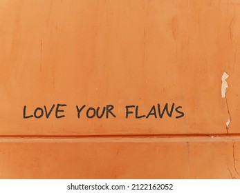 Old grunge orange wall with red text LOVE YOUR FLAWS, concept of positive self talk, learning self love and boost confidence, appreciate and accept our own flaws