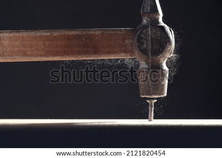 An old hammer hits a nail close-up on dark background. Dust rises from the impact. Carpentry concept.