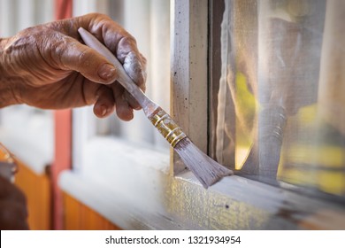 Old man´s hand painting wooden window frame using paintbrush. Repairing exterior of old house. - Powered by Shutterstock