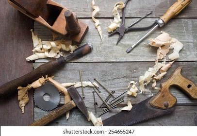 Old hand tools table upper view. Old rusty and dirty carpenter`s hand tools lying on wooden table with sawdust.