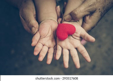 Old Hands Holding Young Hand Of A Baby With Red Heart