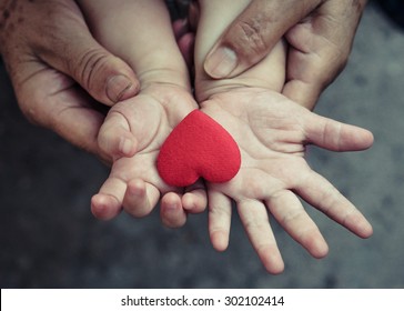 Old Hands Holding Young Hand Of A Baby With Red Heart