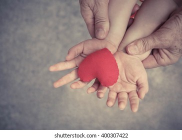 Old Hands Holding Young Hand Of A Baby With Red Heart