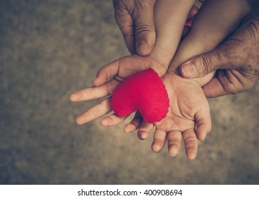 Old Hands Holding Young Hand Of A Baby With Red Heart