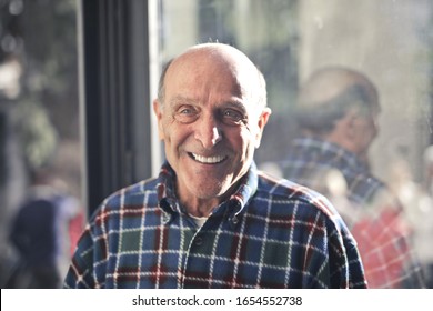 Old Handsome Man Smiling Bright With A Glass In The Background.