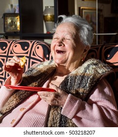 Old Happy Smiling Woman Eating A Slice Of Bread At Home