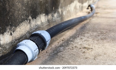 Old HDPE Straight Coupling. Compression Fitting Straight Coupling Connects To Black Plumbing Pipe Beside Concrete Wall With Copy Space. Selective Focus