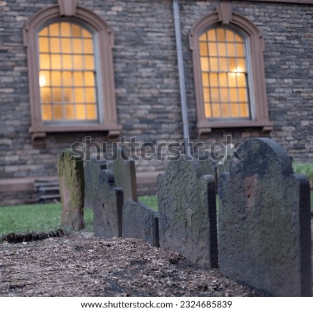 Old headstones in a an church cemetery with church windows in the background.