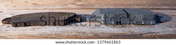 Old, heavily worn rusted brake pad beside a\
brand new brake pad showing the difference in thickness between\
severely worn and new brake pads. Close up on wood background. Side\
by side comparison.