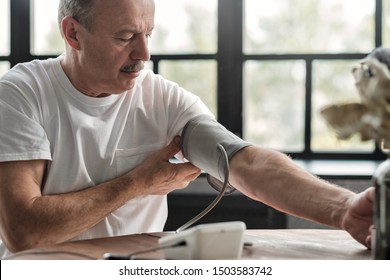 Old Hispanic Man Feeling Bad Using A Home Blood Pressure Machine To Check His Health In The Morning