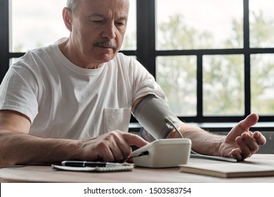 Old Hispanic Man Feeling Bad Using A Home Blood Pressure Machine To Check His Health In The Morning