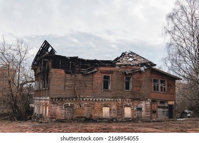 An old historical wooden burnt out house against a gray sky. An abandoned building set on fire.