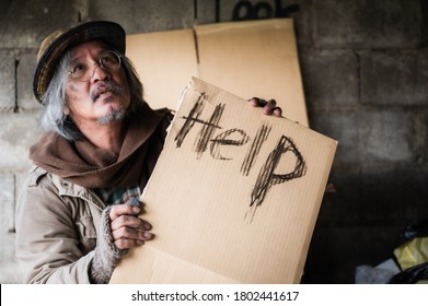 Old homeless man with gray beard sitting hungry and food beggar with holding cardboard sign seeking help from people walking on street. Closeup and focus to word Help on cardboard sign. Hope concept.