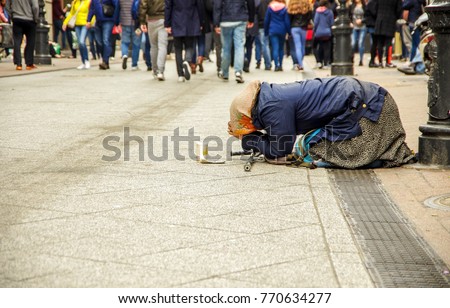 The old homeless woman kneels in the street as passersby pass by and pray for money.