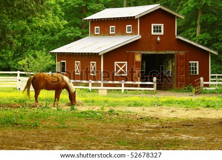 An old horse barn with a horse eating straw in the field in front of it