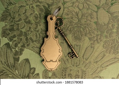 Old Hotel Key With A Vintage Keychain Mockup. Key Is Lying On A Green Jungle Patternd Fabric.