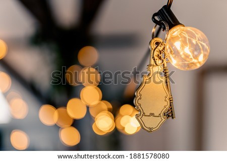Old hotel key with a vintage keychain mockup hanging on fairylights with golden bokeh.