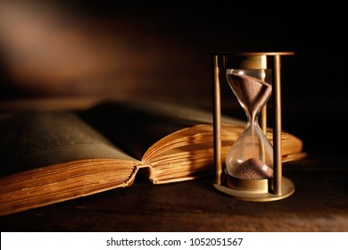 old hourglass with open ancient book
