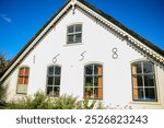 An old house with the year 1658 written on the side wall. On the side wall there are 5 glass windows.