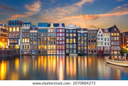 Old houses of Amsterdam in the evening. The houses stand in the water and have a beautiful reflection at night. Touristic district Damrak. These houses are famous all over the world. Amsterdam, Hollan