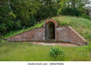 Old Ice House Burried Under A Grass Mound With Red Bricks And Open Gate.