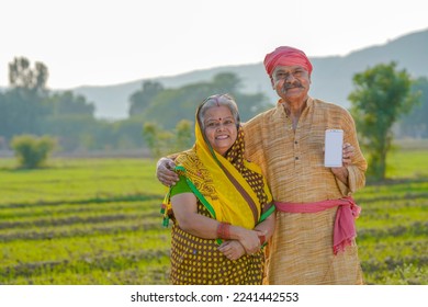 old indian farmer couple standing at agriculture field and showing smartphone.