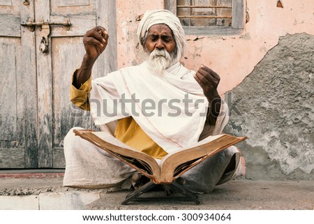 Old indian sadhu (saint) sitting and speak up sacred texts with closed eyes near the temple. 