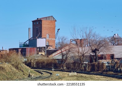 Old Industrial Buildings Next To Railroad Tracks On An Autumn Morning. Red Brick Tower. Pigeons In The Blue Sky Without Clouds. No People. Copy Space.