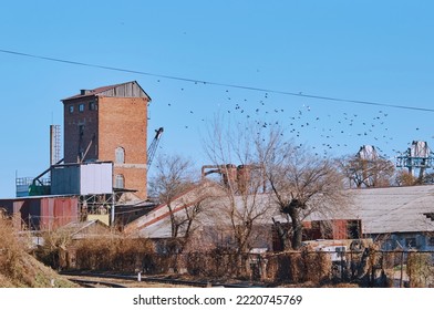 Old Industrial Buildings Next To Railroad Tracks On An Autumn Morning. Red Brick Tower. Pigeons In The Blue Sky Without Clouds. No People. Copy Space.