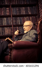 An Old Intelligent Man Reading A Book In His Library At Home. Retirement. Retro Style.