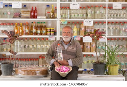 Old Iranian Shop Keeper Holding Rose Water And Fresh Roses And Posing To Be Photographed, Niasar, Iran, April 2019