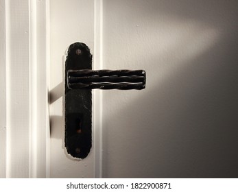 An old iron door handle on a white door.