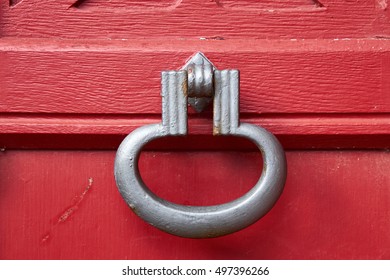 Old Iron Door Knock, Painted With Gray Rust Protection Paint, Fastened To A Red Wood Door.