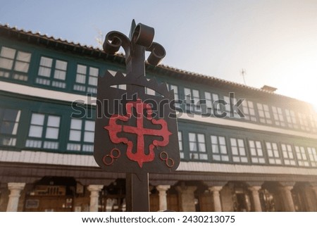 Old Iron Emblem of the Order of Calatrava iluminated by the morning sun. red Greek cross with fleur-de-lis at its ends, in the Plaza Mayor of Almagro, Ciudad Real. Spain