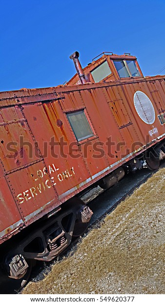 Old iron red train caboose sitting on the tracks\
with a blue sky / Old\
Caboose