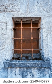 an old iron window with bars, rusty, and a white stone wall