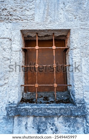 an old iron window with bars, rusty, and a white stone wall
