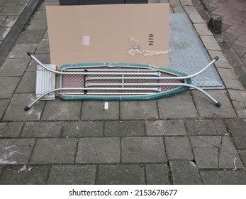 an old ironing board leaning against a waste container on the sidewalk