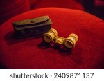 Old ivory vintage theater binoculars lie on red brocade in a theater box, opera glasses, dark holder 