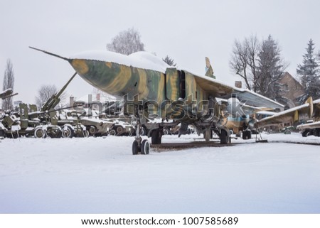 Old jet fighter is covered with snow on the background of military equipment