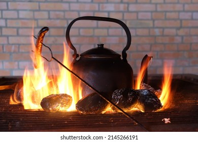 The Old Kettle Is On The Hearth With A Fire. A Sausage Is Baked On Stick.