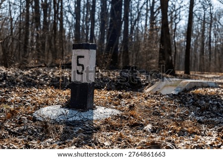 Old kilometer post near abandoned railway tracks in a spring forest, distance marker in the woods.