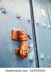An old knocker on the front door of a house in Spain. A green wooden door with a beautiful knocker on the outside. Golden colored knocker in the form of a hand. Traditional door decoration in Spain.