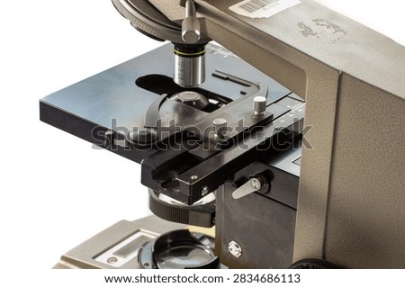 Old laboratory microscope with two objective lenses, eyepiece and metal stage, photographed from a side angle.