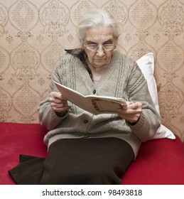 Old Lady (European) Sitting Reading Book At Home.